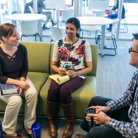 Three colleagues are sitting on a green couch having an informal meeting