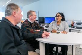 Two men and one woman seated around a round table in an office setting 