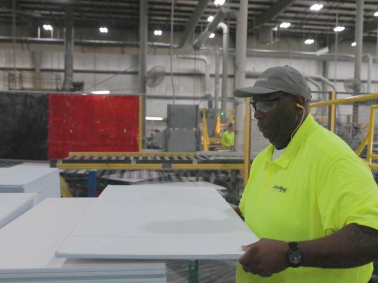 A man wearing a safety yellow color polo shirt inspects a ceiling tile