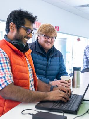 Two men are standing together at a laptop computer in a lobby area
