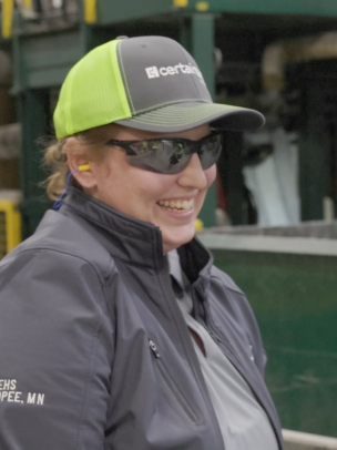 A woman wearing CertainTeed safety gear stands on roofing plant floor