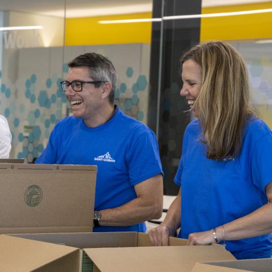 A man and a woman wearing matching company shirts are packing boxes for Good360