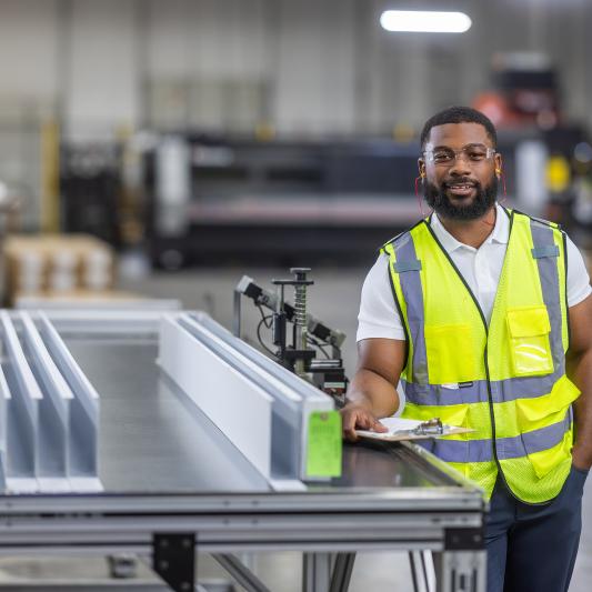 A male employee at a Saint-Gobain North America plant smiles, proud of his successful path in manufacturing and operations jobs.