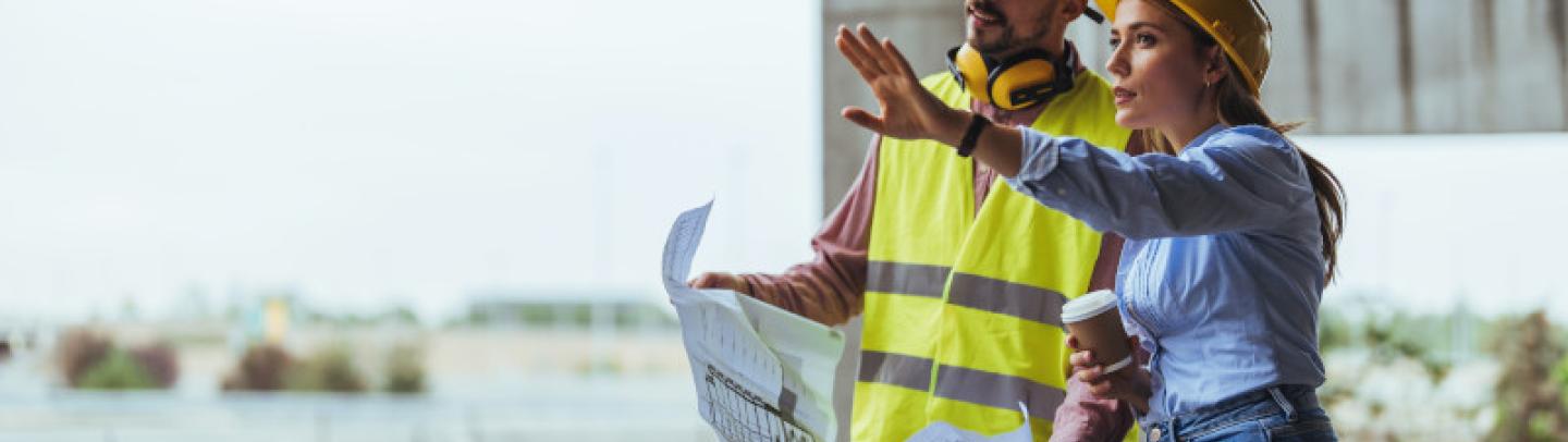 two workers in safety gear looking at blueprints