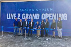 9 people stand in front of a sign that reads "Palatka Gypsum Line 2 Grand Opening" while the female Plant Manager in the center cuts the ribbon