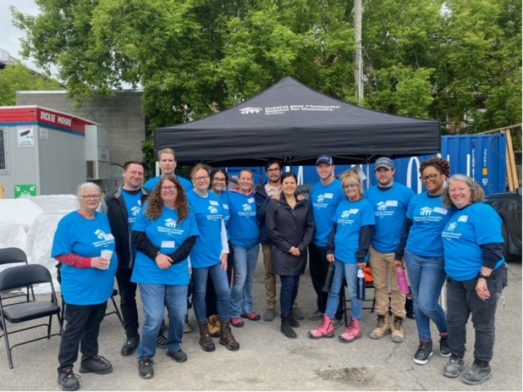 A group of people pose for a photo underneath a Habitat for Humanity tent wearing matching shirts