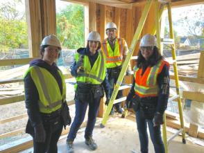 Four people wearing safety gear pause for a photo while building a home