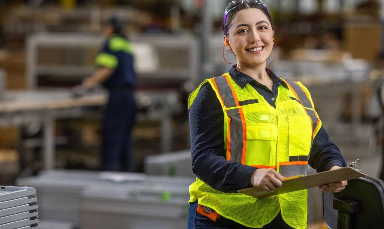 A female professional in a hard hat and safety vest reviews technical data on a tablet, representing the modern career paths in Manufacturing and Operation Jobs near Houston, Texas.