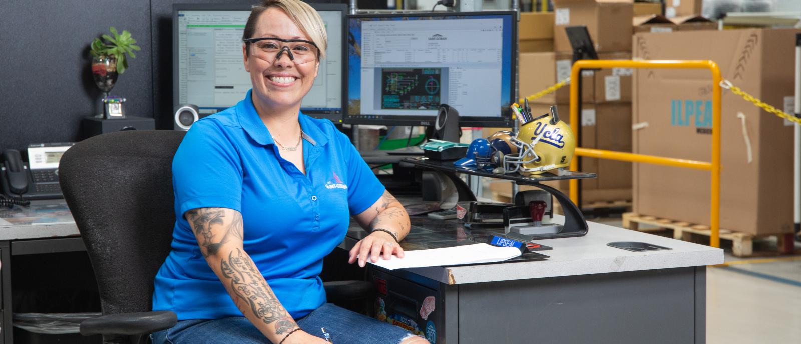 Female employee smiling at her desk, representing administrative roles that support manufacturing and engineering jobs in the USA at Saint-Gobain.