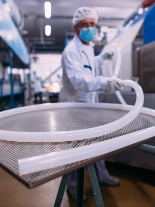 plastic tubing coiled on a metal sheet in a laboratory with a person in full medical PPE holding the end of the tube in the background