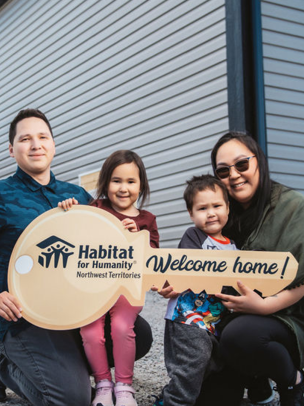 A family holds a wooden key that says "Habitat for Humanity Canada Welcome Home"