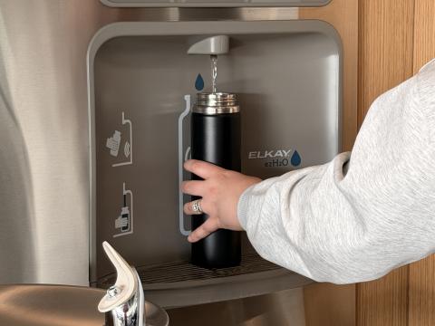 Someone holding a aluminum water bottle is getting water from the fountain